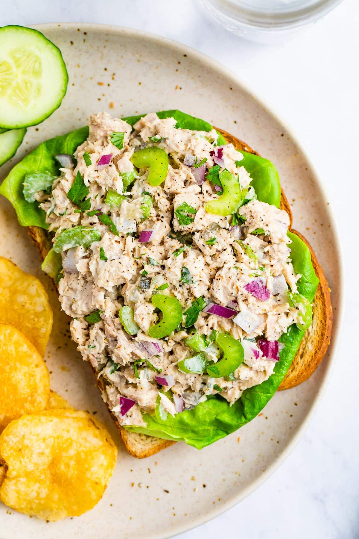 Salada de atum numa sanduíche de cara aberta com alface. Em um prato com batatas fritas e pepinos.