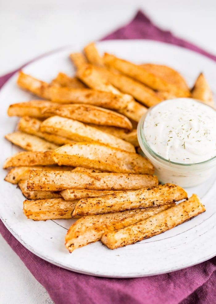 Um prato branco de batatas fritas nabiças e um frasco de molho de rancho em cima de um guardanapo púrpura.