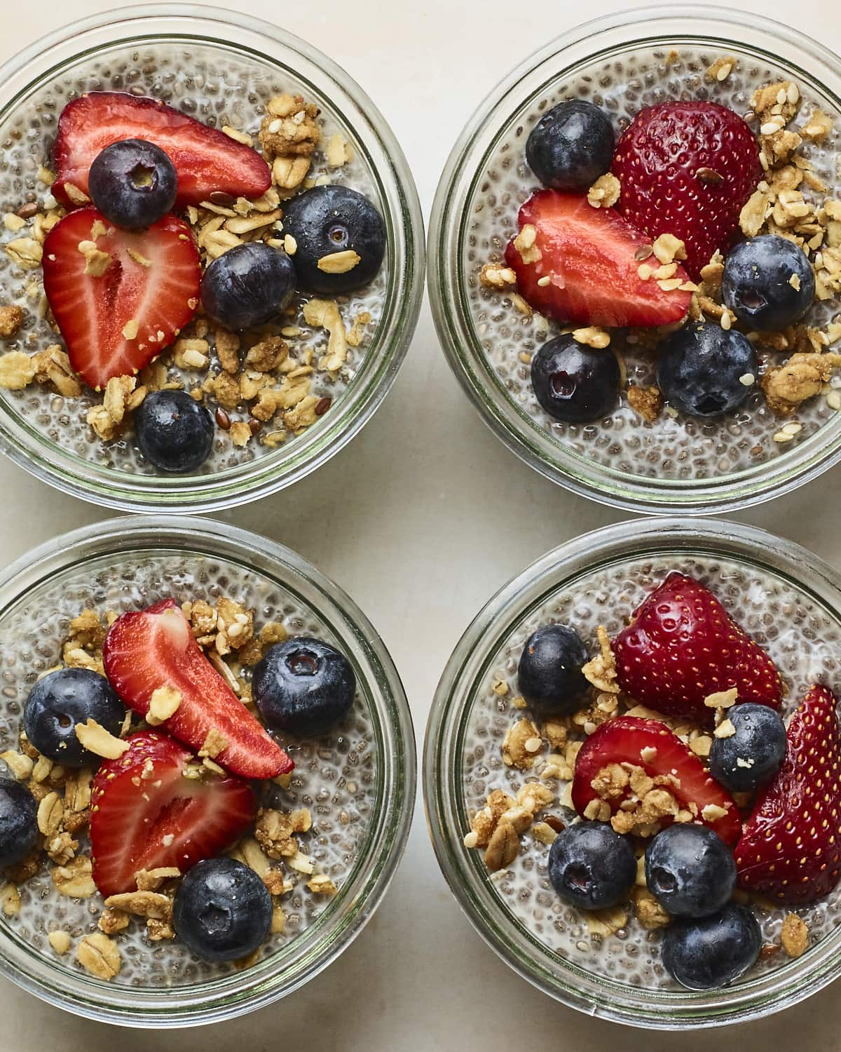 Quatro frascos de vidro com pudim de chia coberto com fruta e granola.