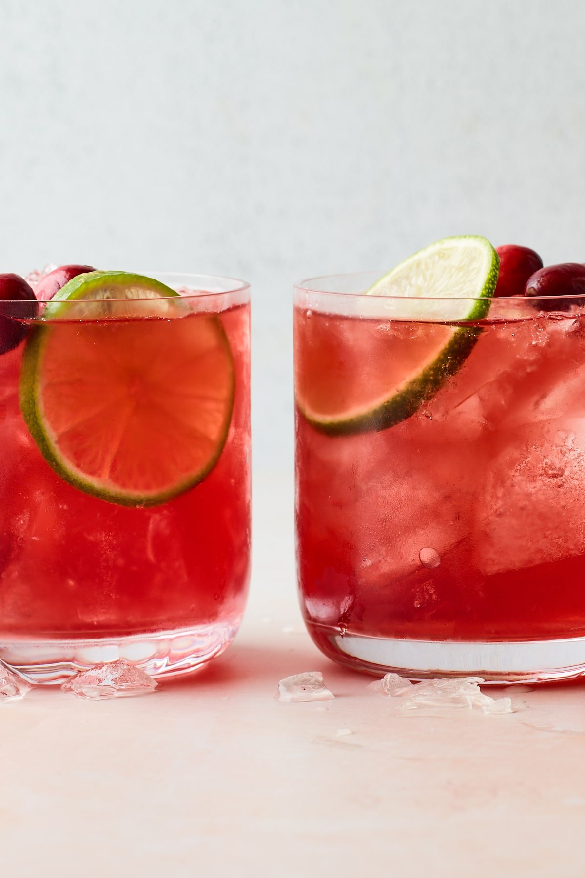 Dois copos cheios de vodka cranberry sobre gelo. Cada um deles foi coberto com uma fatia de lima e alguns arandos inteiros.