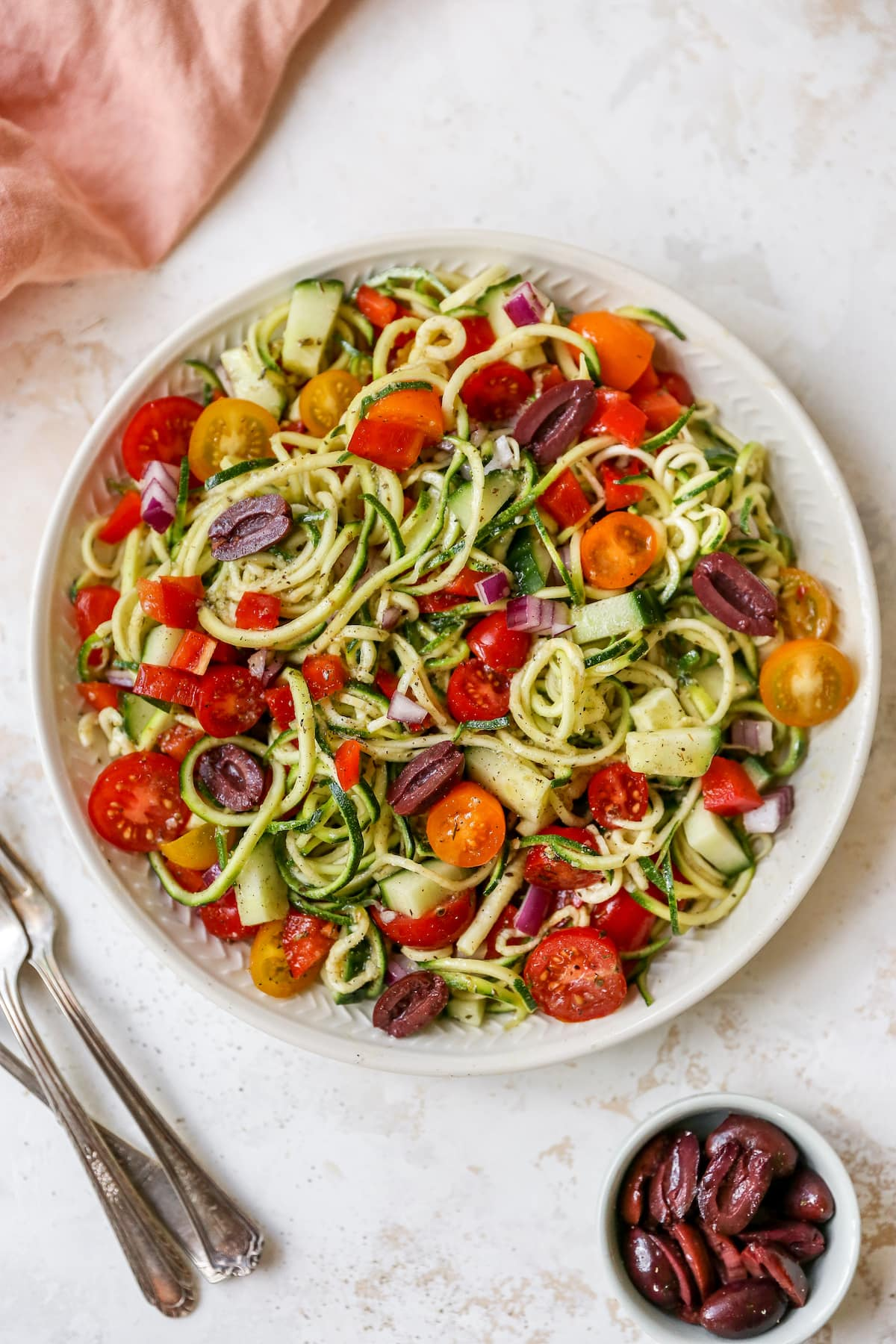 Tigela de salada de massa de abobrinha com tomate, pimentão e azeitonas.